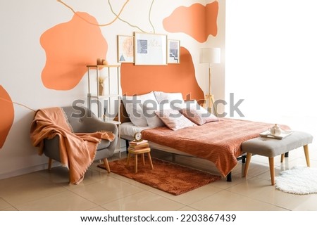Bed with armchair and rack near creative painted wall in room