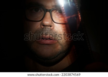 man looks at vintage film in dark room. isolated on black background. Male photograph looking at 35 mm tape. Film photography concept. Film development. vintage hobby. Film photo amateur. archive