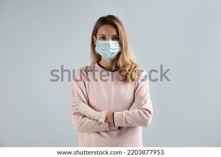 Young woman in medical gloves and protective mask on grey background