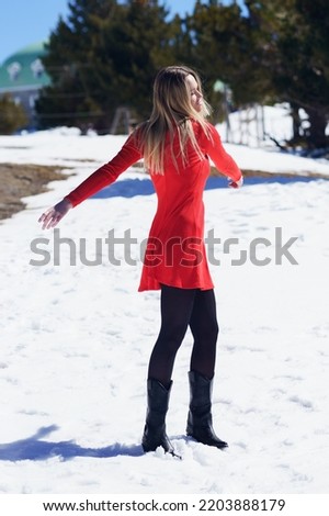 Young blonde woman wearing a red dress and black stockings opening her arms in happiness in the snowy mountains, in Sierra Nevada, Granada, Spain.