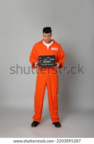 Prisoner in orange jumpsuit with mugshot letter board on grey background Royalty-Free Stock Photo #2203895287