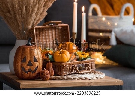 A wicker basket with pumpkins, Jack's Pumpkin and candles in the interior of the living room on a wooden table. The concept of home comfort. Autumn decor for Halloween. Royalty-Free Stock Photo #2203896229