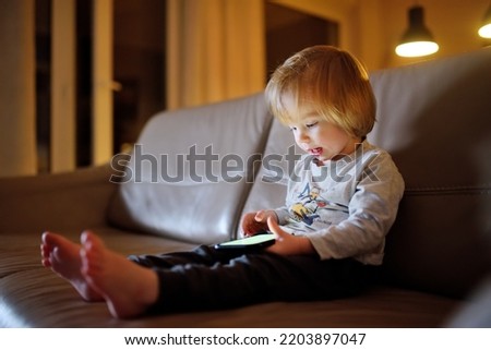 Adorable toddler boy playing with a smartphone in a dark room. Child holding mobile phone. Education and learning for small kids.