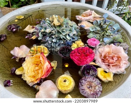 A bird bath that is filled with fresh, clean water and different types of picked flowers. The inside of the tub has leaves engraved into it.