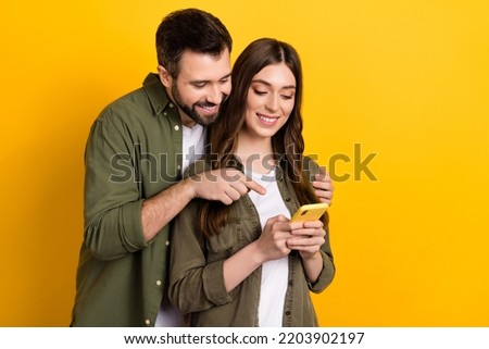 Photo of cheerful couple surfing internet together choose clothes from online shop isolated on yellow color background
