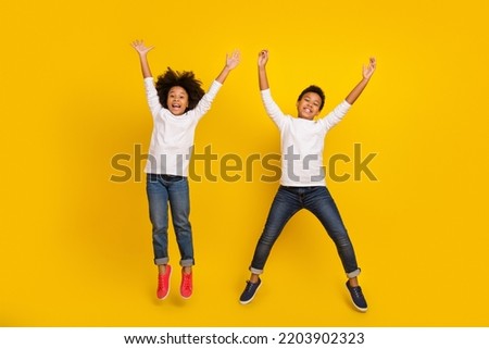 Photo of funky excited schoolboy schoolgirl wear white shirts jumping high rising arms isolated yellow color background Royalty-Free Stock Photo #2203902323