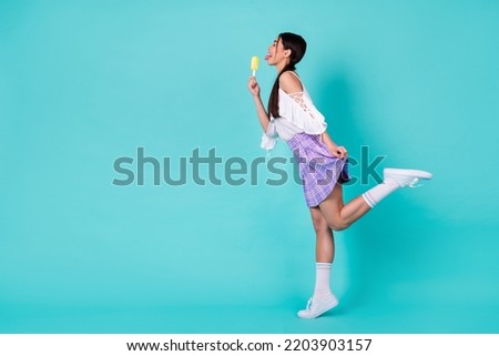 Full size profile side photo of student lady lick fresh popsicle wear short mini skirt long socks isolated cyan color background