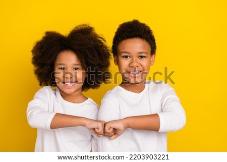 Portrait of two positive buddies give fist bump each other toothy smile isolated on yellow color background