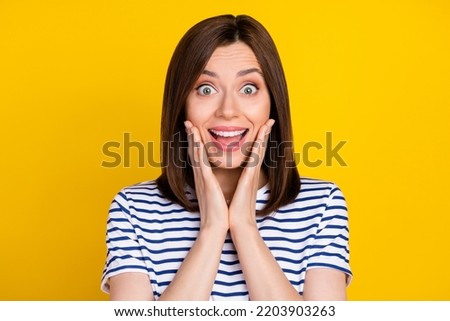 Portrait of gorgeous impressed nice girl with bob hairstyle dressed striped t-shirt palms on cheekbones isolated on yellow color background