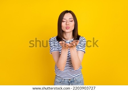 Photo portrait of nice young woman closed eyes send air kiss romantic mood dressed trendy striped look isolated on yellow color background