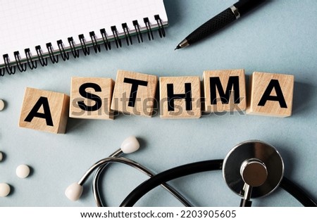 Wooden cubes with the inscription ASTHMA lie on the table. View from above. Nearby is a stethoscope, a notebook and scattered pills.