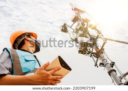Asian male engineer safety helmet works in the field  high rise building inspecting telecommunication tower structures setting up electronic power grids and maintaining 5G networks for safety reasons. Royalty-Free Stock Photo #2203907199