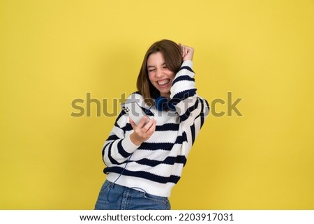 Portrait of cute happy teenage girl wearing talking on mobile phone and smiling  over yellow background. Copy space.