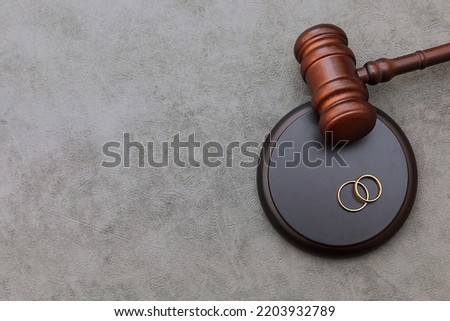 Law theme. Judge gavel wedding rings on concrete stone grey background. Divorce proceedings. Mallet of judge deciding on marriage divorce, marital agreement, legalities of divorce Royalty-Free Stock Photo #2203932789