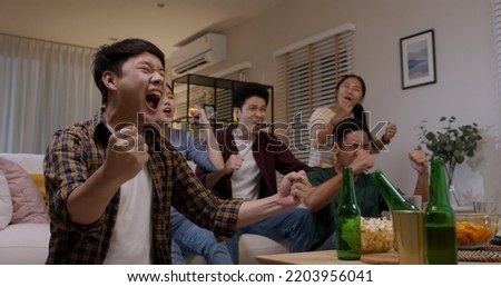 Group of young adult friend man and woman asia people sit at sofa couch joy night party fun game FIFA world cup live TV at home eat snack bowl drink beer bottle glass jump mad happy win exult face. Royalty-Free Stock Photo #2203956041