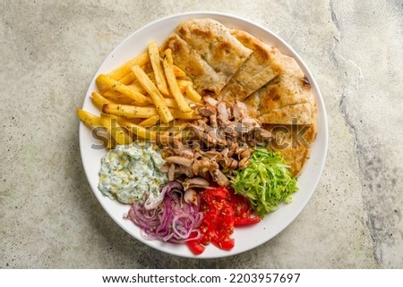 Gyros on plate with chicken, french fries,vegetables and greek sauce top view on stone table
