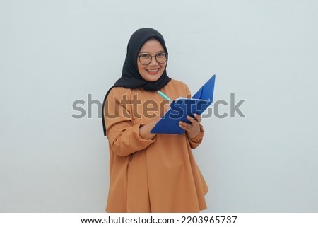 happy muslim woman writing something in book