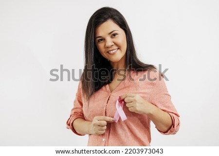 Young Brazilian woman holding breast cancer ribbon over white background Royalty-Free Stock Photo #2203973043