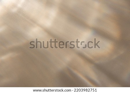 Glowing reflections of the sun's rays on a beige background. Overlay effect of penetrating natural, transparent, soft light and shadows from window on sand color wall texture. Trendy, creative concept