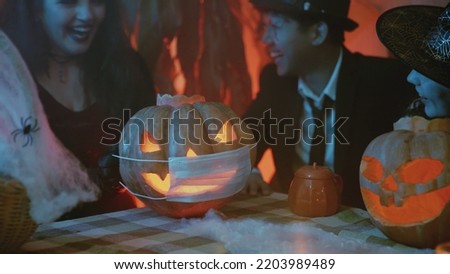 A group of friends celebrates Halloween, puts a medical mask on a Jack-o'-lantern and laughs loudly. Close-up