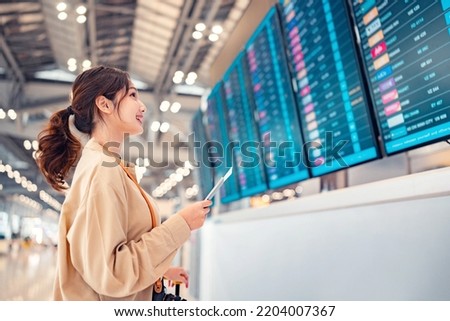 Happy asian woman traveller checking flight schedule departures board in airport terminal hall in front of check in counters. Tourist journey trip concept Royalty-Free Stock Photo #2204007367