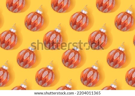 Repetitive pattern made of gold colored Christmas baubles on a yellow background.