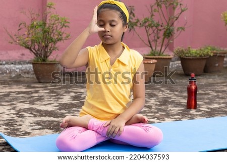 An Indian girl child practicing pranayama anulom vilom on yoga mat outdoors Royalty-Free Stock Photo #2204037593