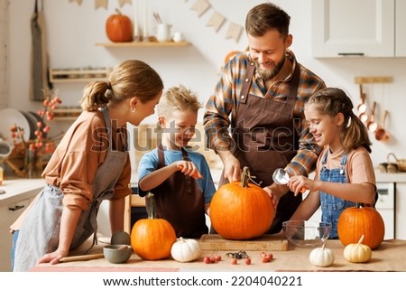 Happy family mother, father  and children daughter and son to remove   pulp from pumpkin while carving jack o lantern with family in cozy kitchen at home, parents with kids preparing for Halloween