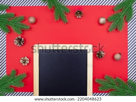 Black chalk board for announcement with spruce branches, golden cones and walnuts, glitter balls on red background and striped. Christmas, New Year flat lay. Copy space