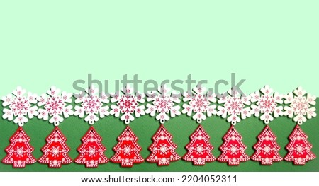Christmas background for writing text or a congratulatory letter.  On a green background, white wooden snowflakes and red Christmas trees, a symbol of the new year.  Space for copy text.