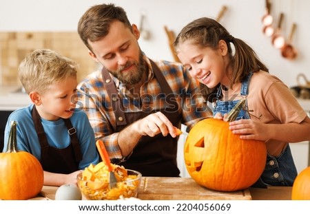 Happy kids boy and girl helping father to carve Halloween pumpkin while standing in kitchen at home and preparing for autumn holiday, family children and dad making Jack-o-Lantern together