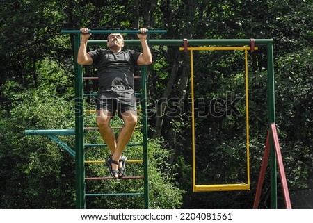 athletic man performs pull-up exercises on the horizontal bar in the children's outdoor area