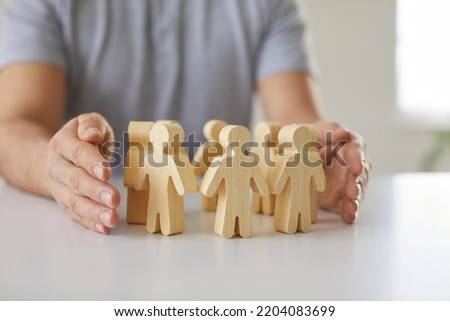 Man guarding small wooden human figures. Close up of male hands and little pawn people on desk. Responsible team leader creates safe workplace and protects his employees. Corporate safety concept