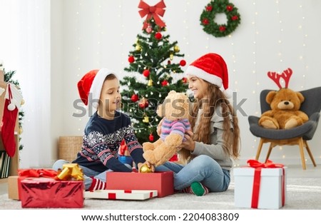 Smiling children celebrate New Year at home unpack presents together in living room. Happy boy and girl kids have fun open gifts on Christmas morning, enjoy winter holidays festive atmosphere.