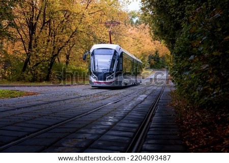 A modern-style tram goes out of a dense forest in autumn colours, Moscow, Russia Royalty-Free Stock Photo #2204093487