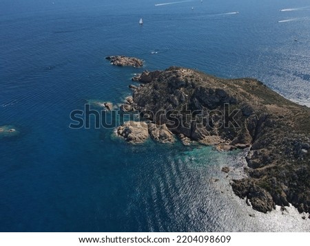 Aerial view of Plage Ranc and Cap Taillat in French Riviera, near Saint-Tropez. Beautiful rocky beach near coastal path with luxury yachts, turquoise and idyllic water. Drone view from above France.
