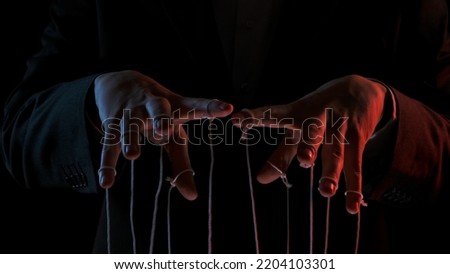 Male hand with marionette strings on black isolated backgorund. Boss in a black business suit controlling managers. Concept of dictatorship and control of the government of the people. Close up. Royalty-Free Stock Photo #2204103301