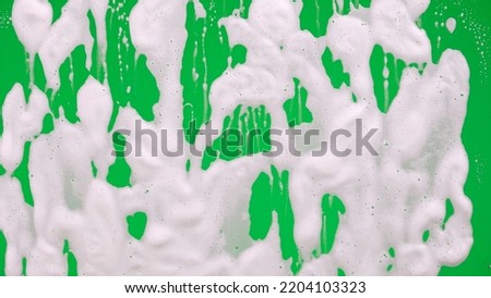 White soap foam with bubbles flowing down the window glass on green screen chroma key background. Cleaning windows with cleaning disinfectant. Hygiene, disinfection, housework, household. Close up.
