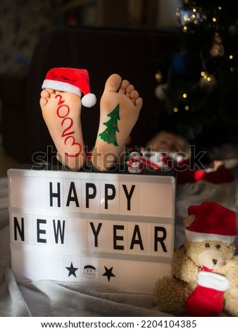 concept of preparing for Christmas. positive, pampering, humor. numbers 2023 are written on child's bare feet. inscription happy new year. festive cozy pictures on New Year theme