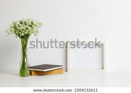 Book, white flowers and white frame over the white wall.