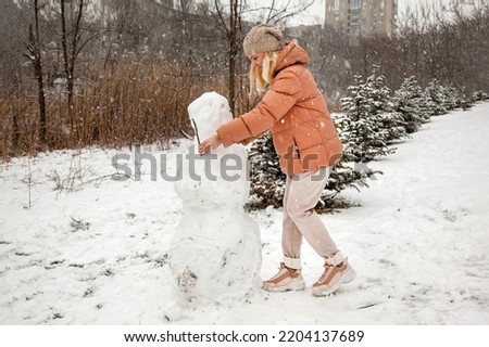 Woman makes a snowman in a city park during a snowfall.