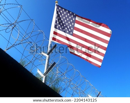 The American flag hangs in the cloudy sky outside the prison's barbed wire. waving in the sky