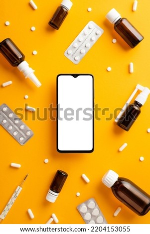 Healthcare concept. Top view vertical photo of smartphone spray and syrup transparent brown bottles tablets capsules and thermometer on isolated orange background with copyspace