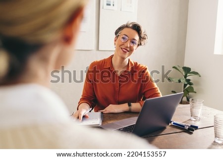 Happy hiring manager smiling while interviewing a job candidate in her office. Cheerful businesswoman having a meeting with a shortlisted job applicant in a creative workplace. Royalty-Free Stock Photo #2204153557