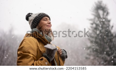Young mature adult caucasian woman in a hat and yellow jacket breathing fresh air in the winter forest Royalty-Free Stock Photo #2204153585