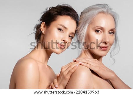 Two smiling women of different ages looking at different side holding hand closeup portrait. Young girl cuddling snuggling mom from back.  Relation between parent and adult kid Royalty-Free Stock Photo #2204159963