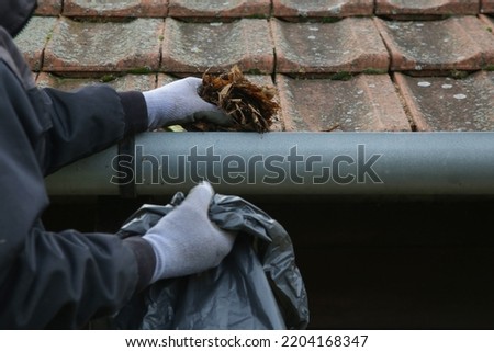 Cleaning the gutter from autumn leaves before winter season. Roof gutter cleaning process.	 Royalty-Free Stock Photo #2204168347