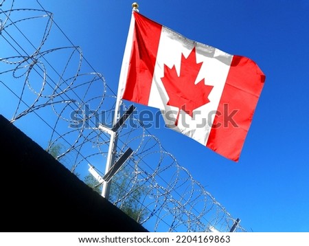 The Canadian flag hangs in the cloudy sky outside the prison's barbed wire. waving in the sky