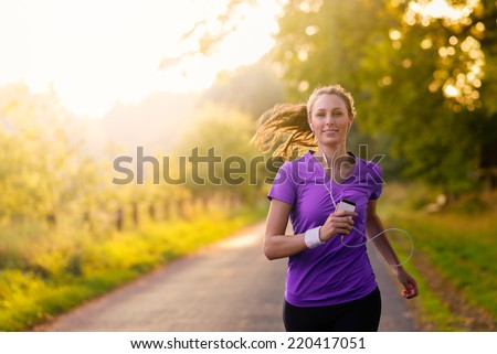 Woman listening to music on her earplugs and MP3 player while jogging along a country road in a healthy lifestyle, exercise and fitness concept Royalty-Free Stock Photo #220417051