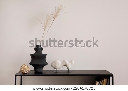 Minimalist composition of sitting room interior with black commode, vase with dried flowers, book, sculpture and personal accessories. Beige wall, copy space. Template.	